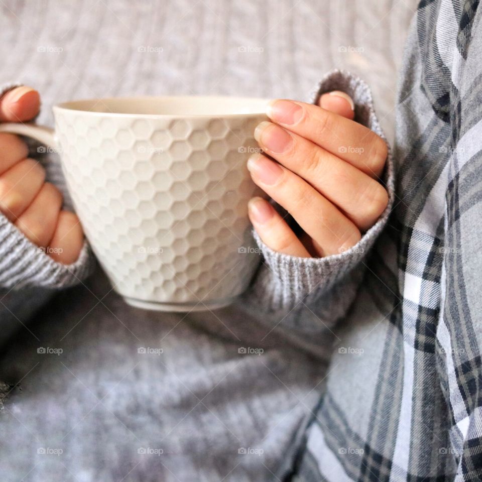 Hand and holding grey mug against grey jumper and grey pj bottoms. 