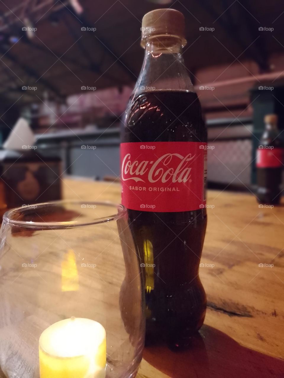 coca cola en botella pequeña junto a un velita en bar de noche