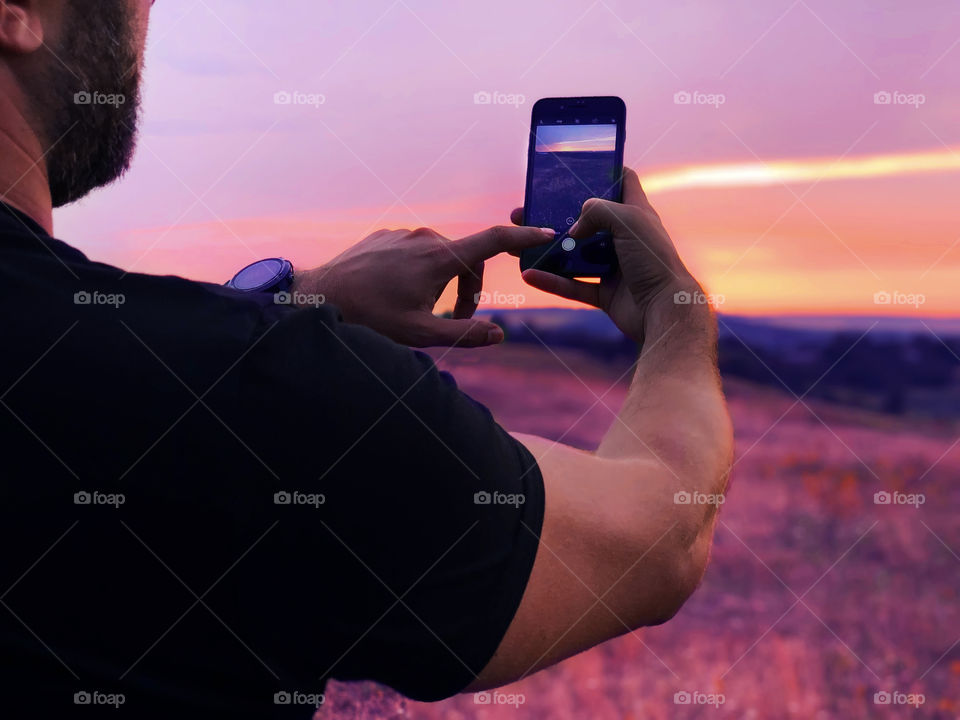 Young man taking a photo of a beautiful purple sunset 