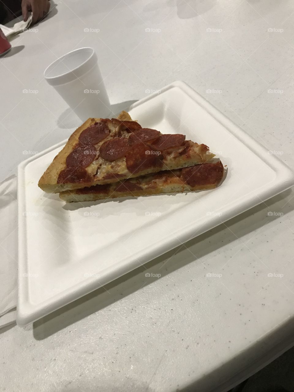 It is pizza dinner at church. Two slices of pepperoni pizza would undeniably satisfy one’s appetite. There is a cup of water to go with the meal. It would wash down the pizza.