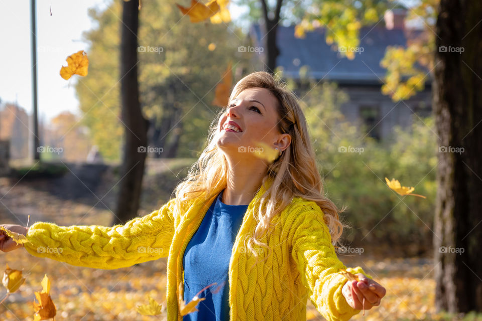 A young, beautiful, blonde woman walking through the autumn park and rejoice in colorful tree leaves.