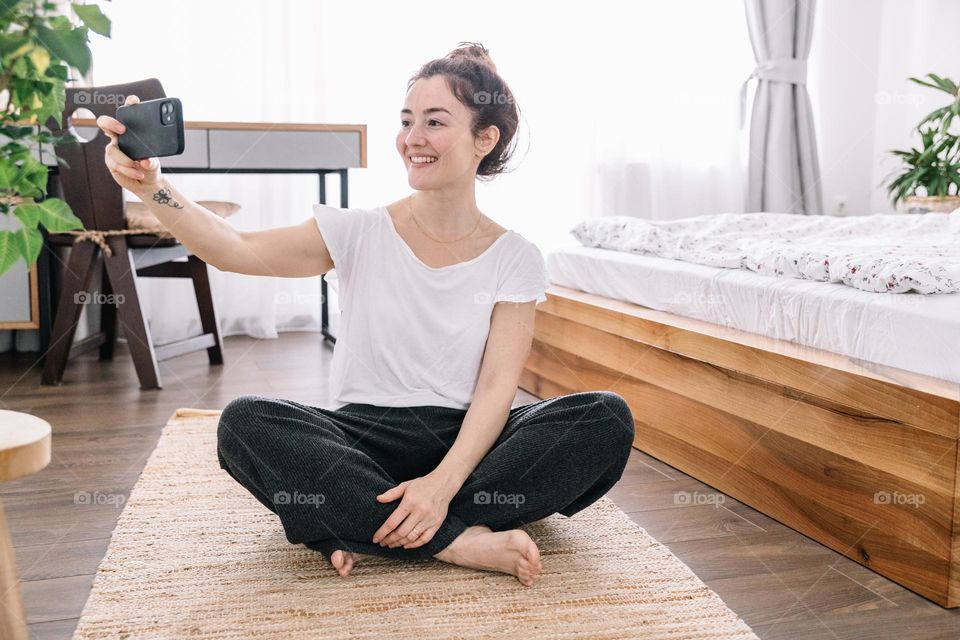 Young woman using her phone to take photos for her social media accounts, while at home.