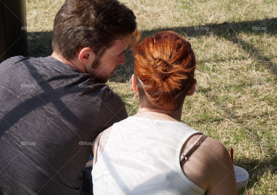 Young love. Couple sitting on the grass lean into each other while talking.