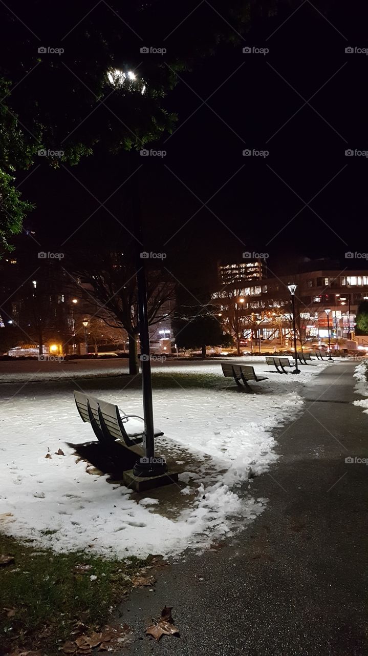 snow covered park and benches at night time