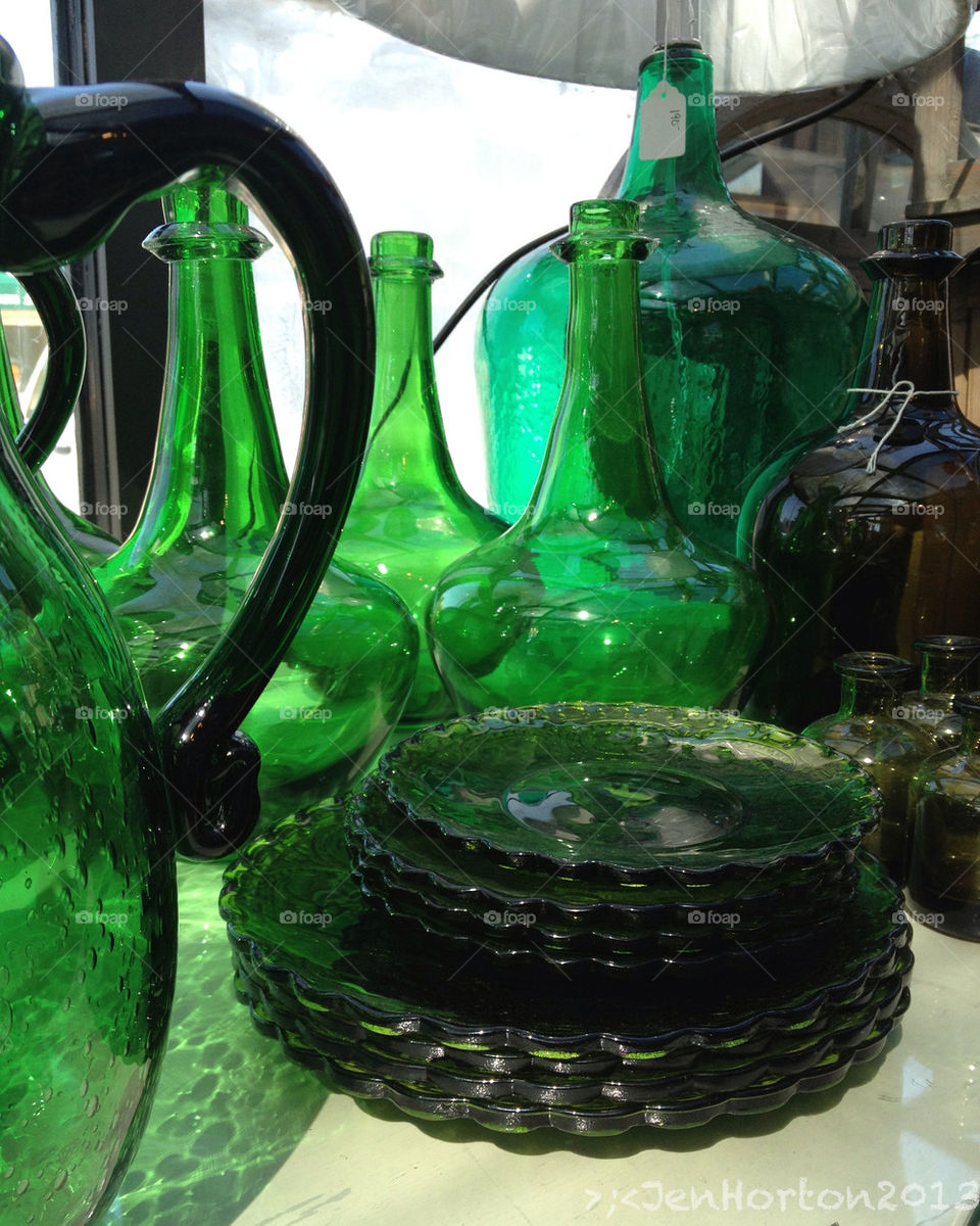 Green glass objects backlit from a sunny window in a small soap shop