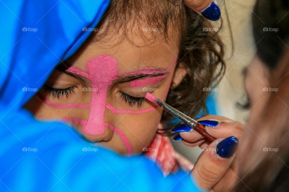 Little girl is getting her face painted. Adding a grime, makeup butterfly on her face