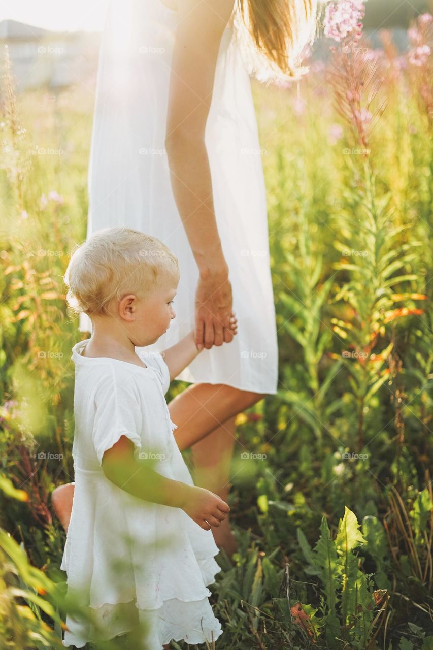 Young woman mother with little girl baby in field on sunset 