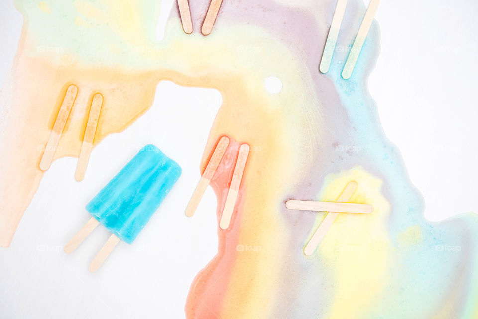 Flat lay of a frozen popsicle surrounded by other multicolored melted popsicle sticks