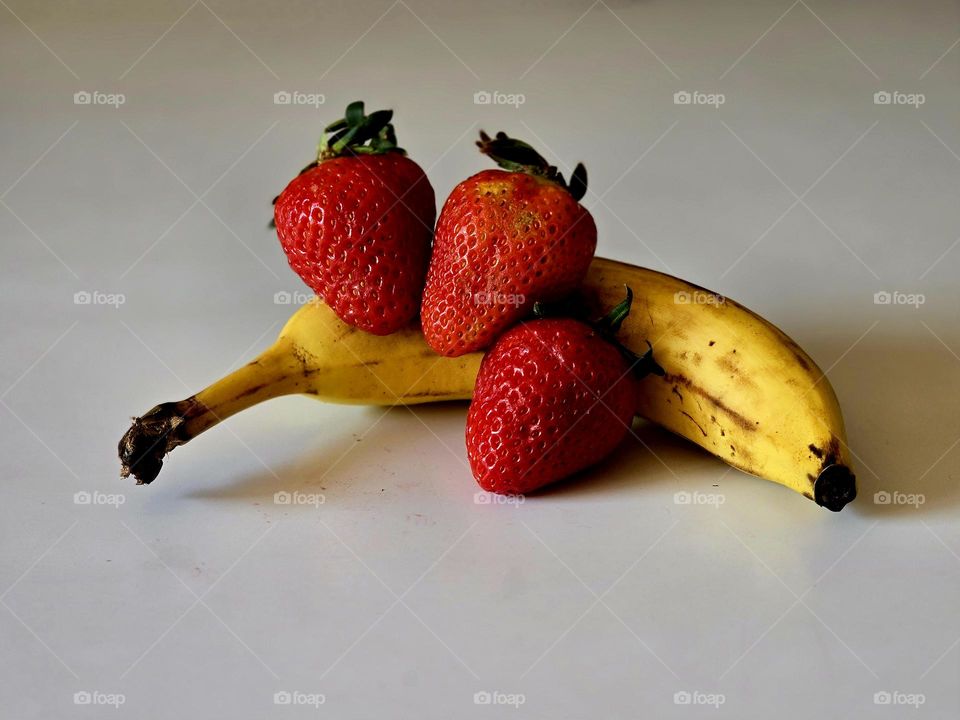 A banana and some strawberries placed on a table with a white background.