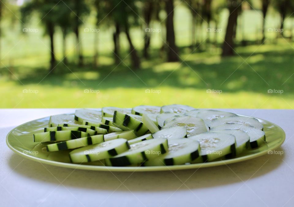 Healthy Living - cucumber slices arranged in a spiral pattern on a green plate on a white table outdoors
