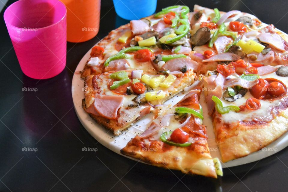 Delicious pizza with meat, veggies and colourfull drink cups 