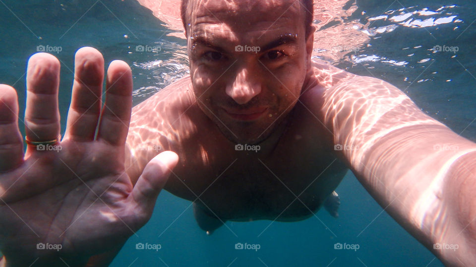 Man diving, man underwater smiling and relaxing in big blue sea
