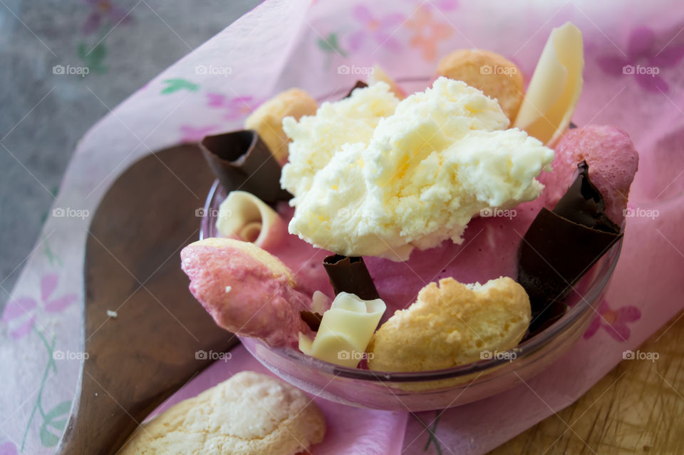 Making Vanilla and Strawberry Ice Cream Charlotte dessert  with homemade lady fingers and dark chocolate in glass bowl on pink background with wooden spoon conceptual classic variations epicure photography 