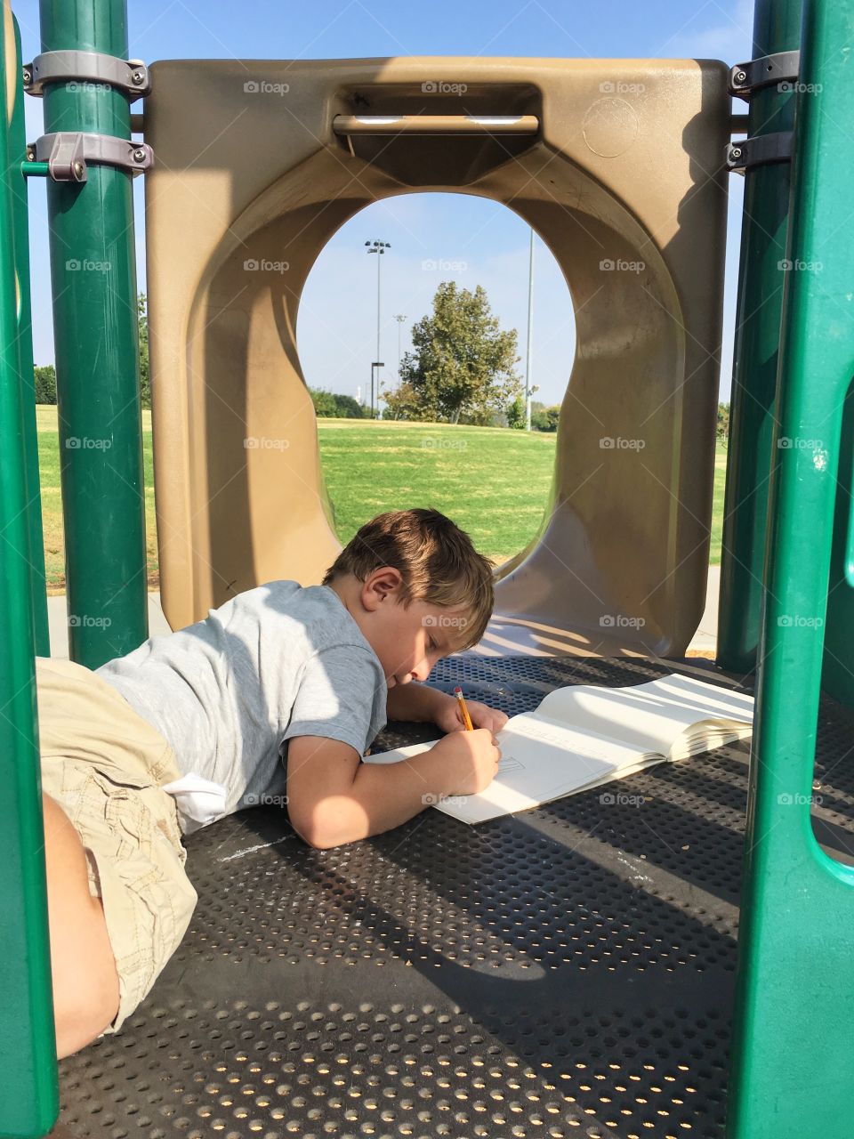 The child is drawing a picture after playing hard. Time for a little rest while drawing on the top of the slide. 