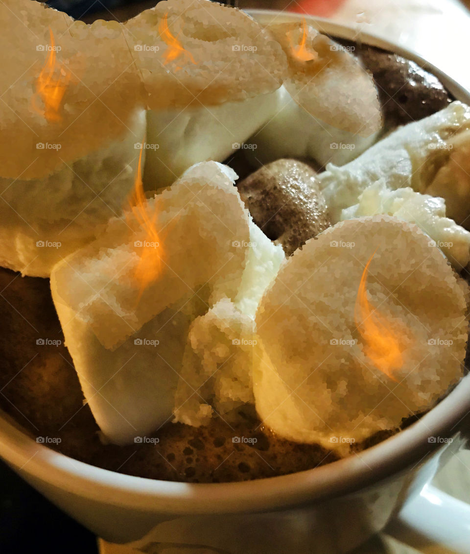 Closeup of a steaming cup of homemade dark hot chocolate with some flaming marshmallows brûlée. (toasting assisted with desktop tools)