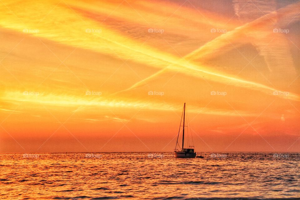 A lone boat floating at sea under an orange sky.