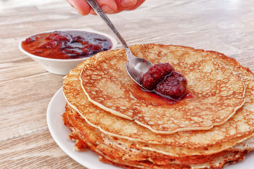 Juicy ruddy hot flavored pancakes with strawberry jam - an amazing dessert. Plate with pancakes on a wooden background.