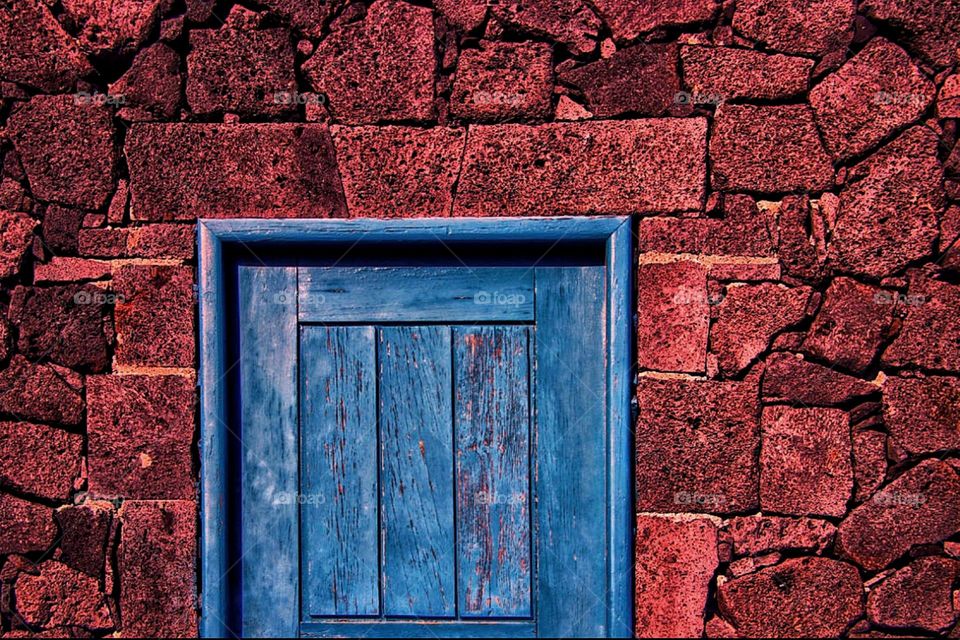 A blue wooden door in a red stone wall