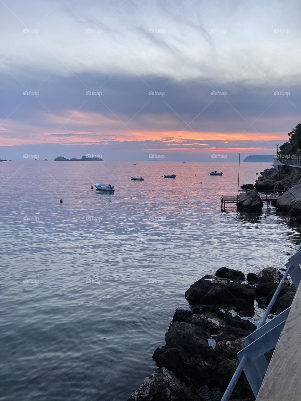 Calm seaside sunset with boats and orange and blue sky.