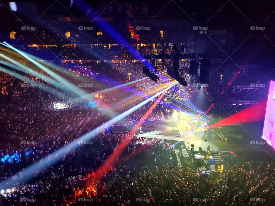 A stadium concert is lit up with colorful lasers and directional lighting