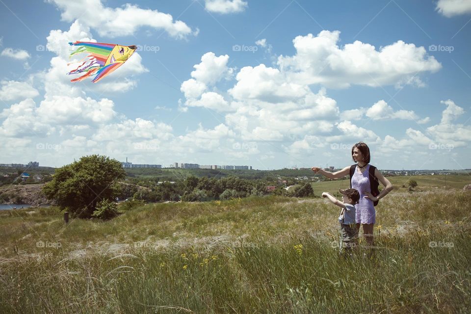 A mother and son together launch a rainbow-colored kite into the sky, a joyful scene of family bonding and outdoor fun