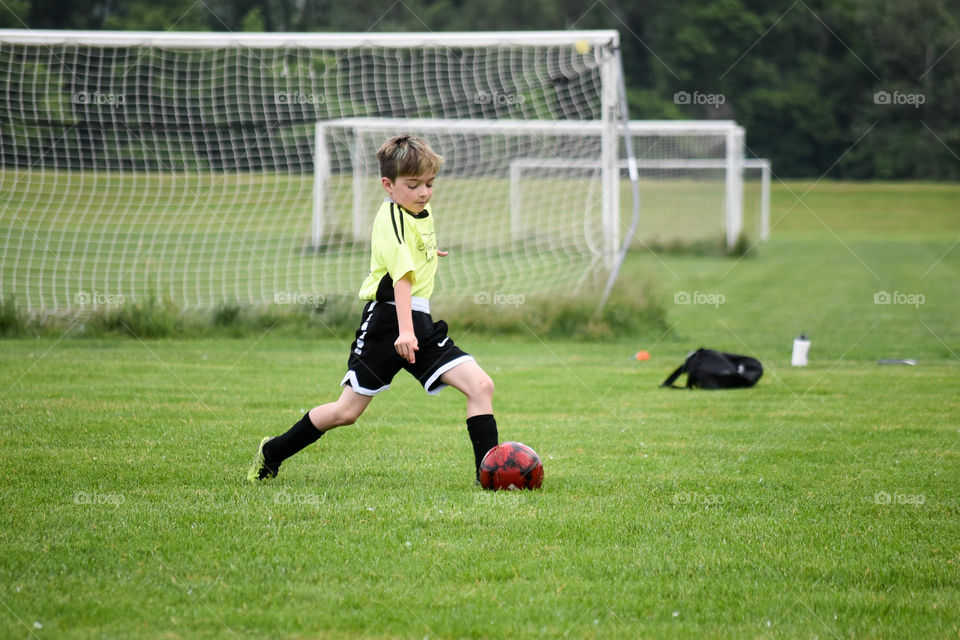 Young boy wearing a jersey and kicking a soccer ball on a soccer field