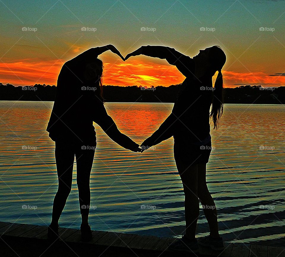 Two life long friends friends make a heart encompassing the magnificent sunset. The loving friendship for each other speaks volumes. Friends for life!