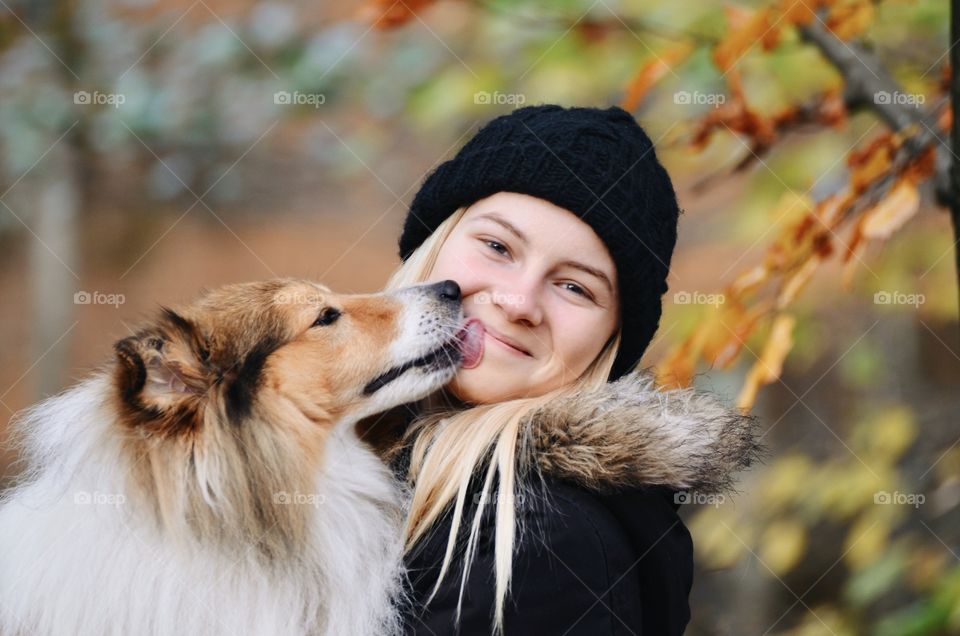 Portrait of a young woman or girl getting a kiss of a Sheltie Shetland Sheepdog dog outdoors in autumn