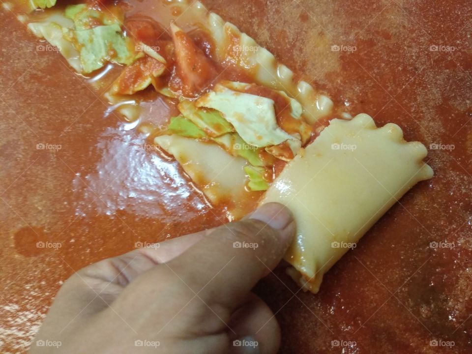 Vegan lasagna roll up on process with hand rolling it up over sauce