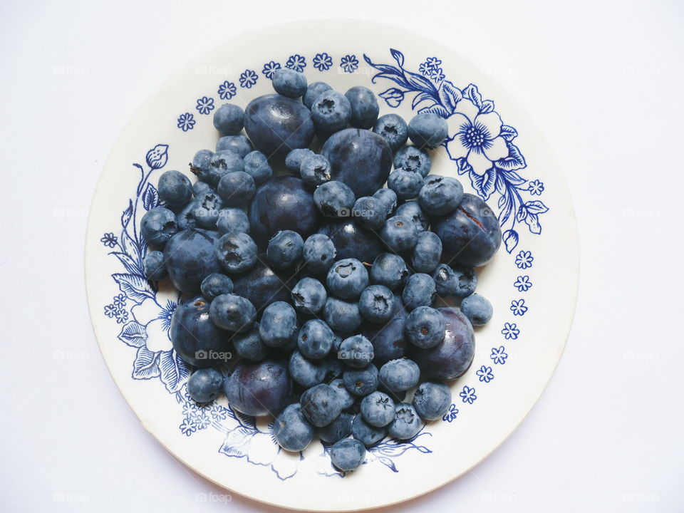 Berries of blueberries and plums on a white plate