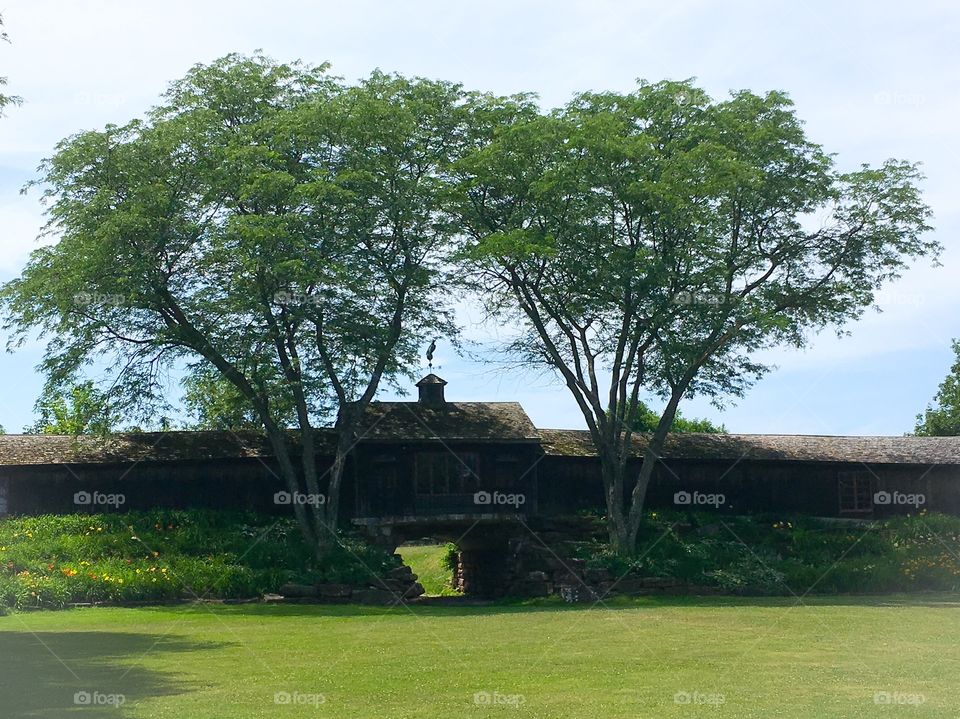 Framed. Two large trees frame the middle section of this wooden building .  Expansive green lawn in the front. 