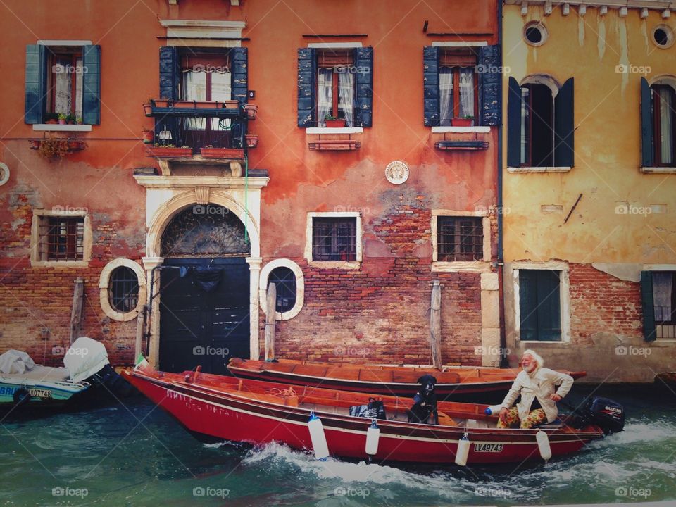 Happy smiling man having a walk down the channel in Venice with his dog in gondola. 