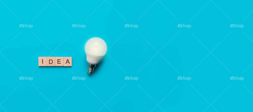 Word Idea formed from wooden letters with illuminated light bulb on blue background. Idea concept. Top view. Banner