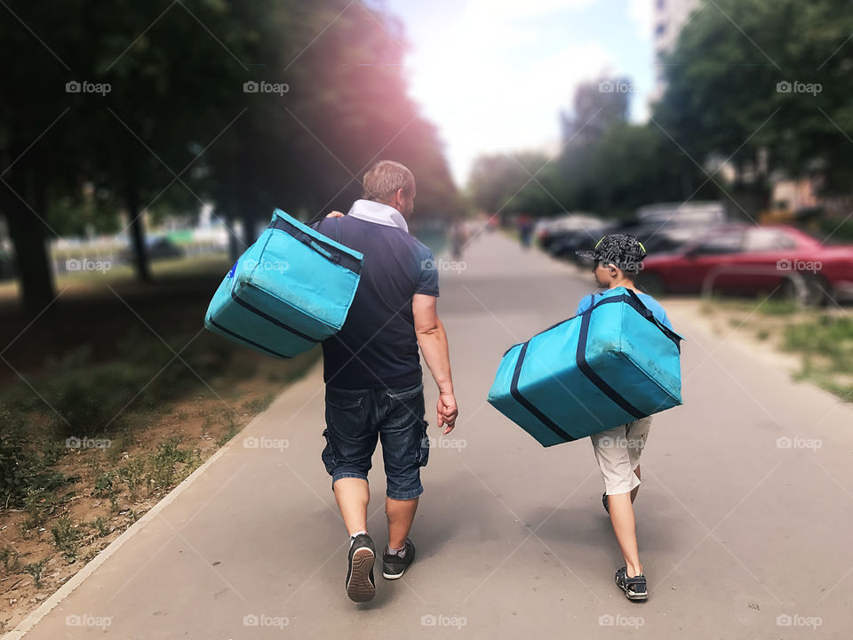 Father and son walking together with luggage through the city road during the moving day
