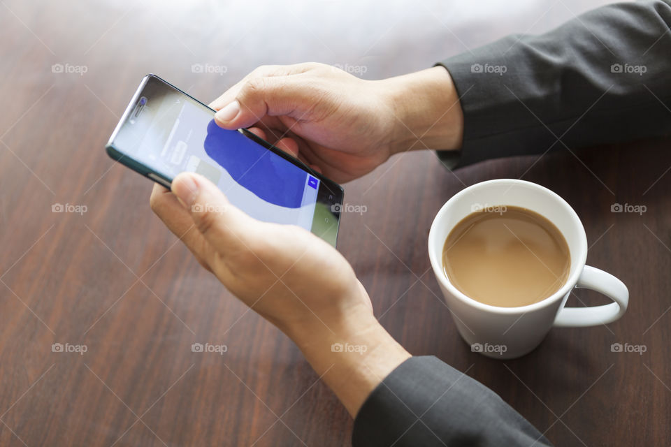 coffee cup beside businessman hands holding smartphone