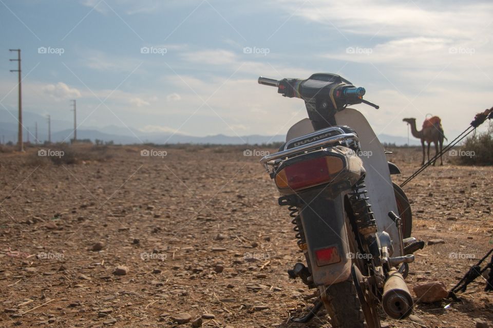 A motorbike in a barren desert with a camel in the background