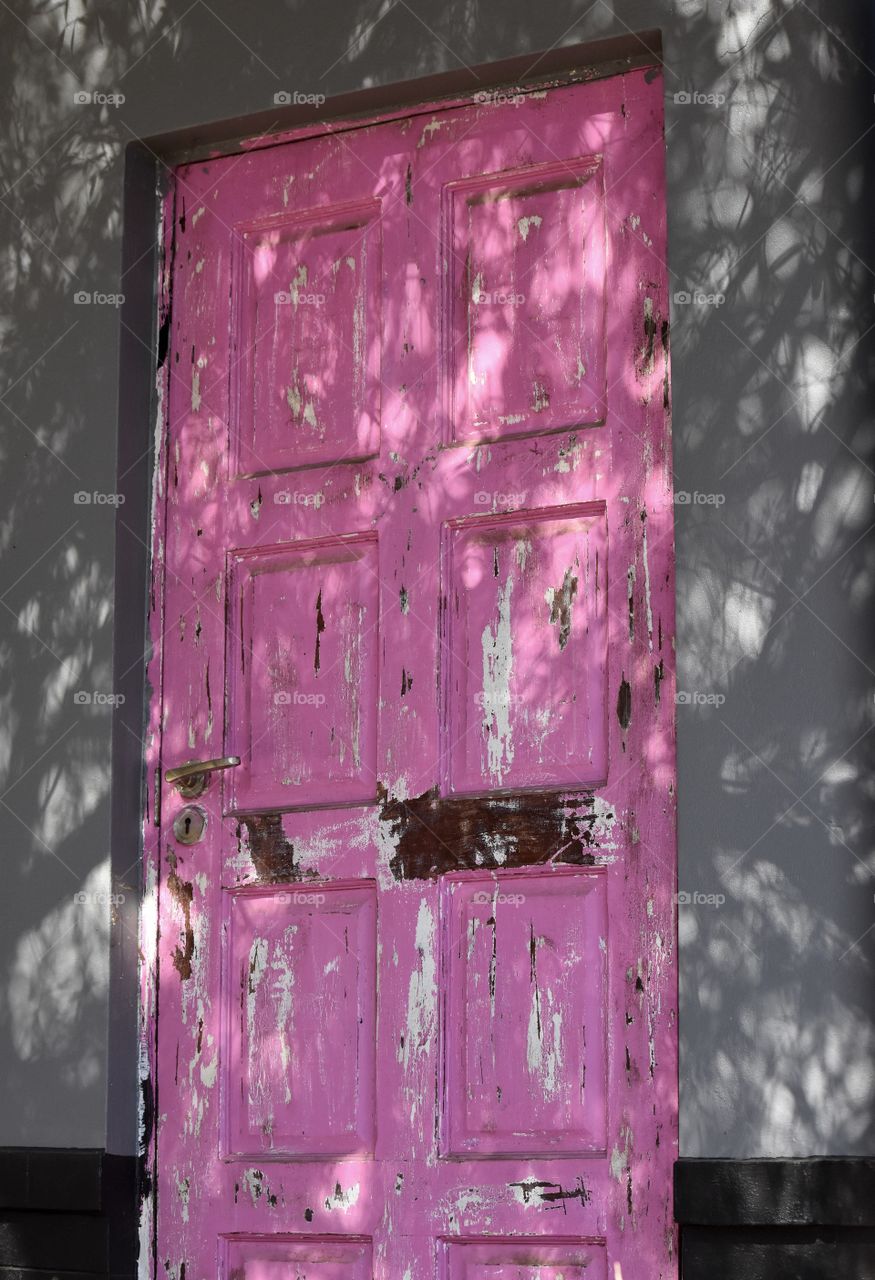 Bright pink, aged door with brown marks against a medium dark gray wall, brass door handle