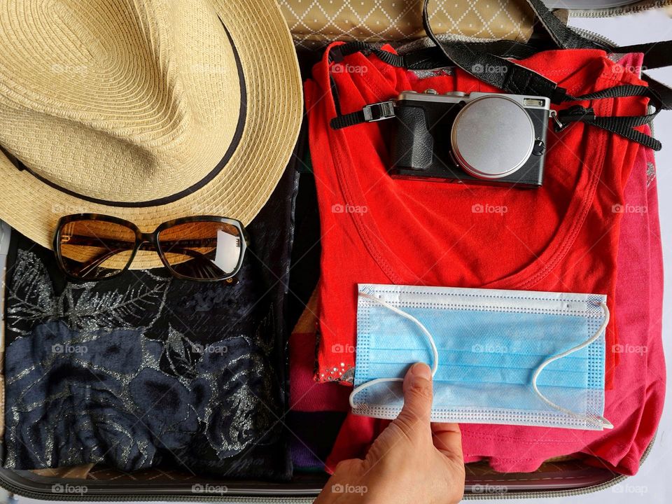 open suitcase with holiday accessories and anti covid surgical mask