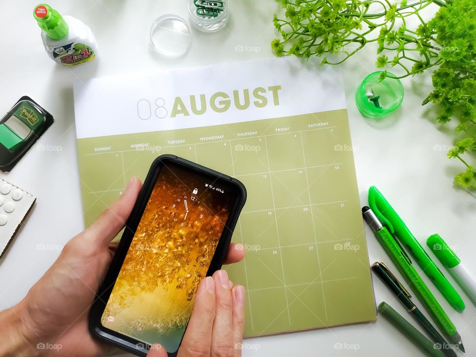 Hands holding a Samsung phone in front of a traditional calendar and desktop stationary.