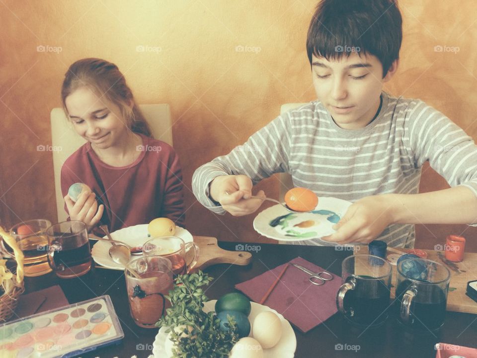 Brother and sister painting Easter eggs at home