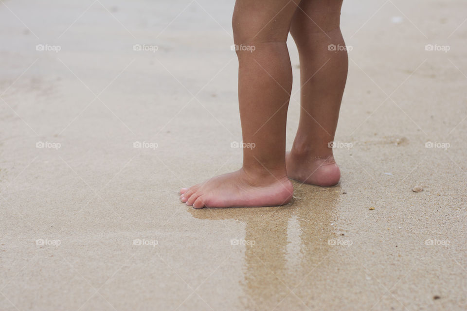 child feet in sand. child is standing barefoot in sand near water on beach
