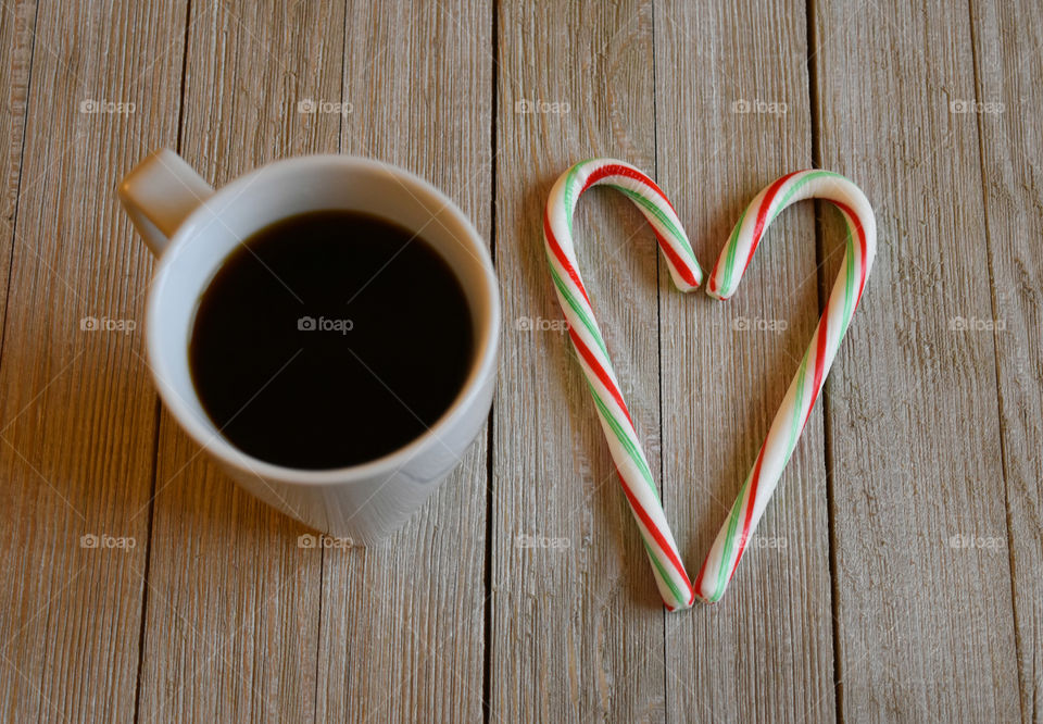 Candy canes in the shape of a heart with a cup of coffee on wood background