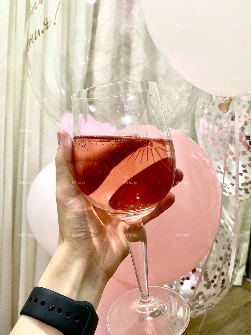 In the photo there is a girl’s hand with a glass of drink against the background of balloons