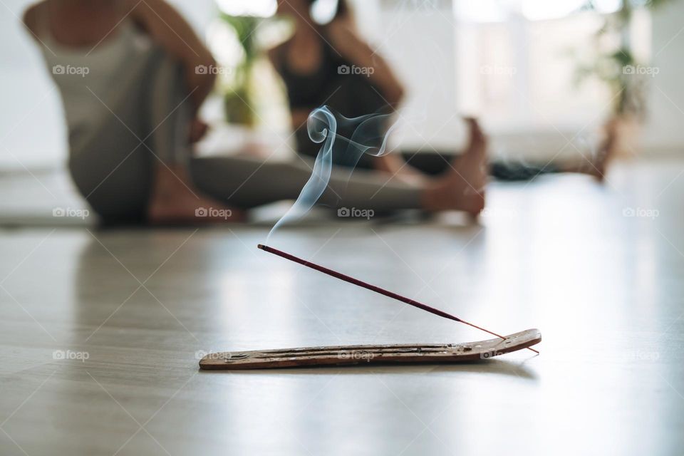 Smoking aroma stick on background of women practice yoga in a bright yoga studio