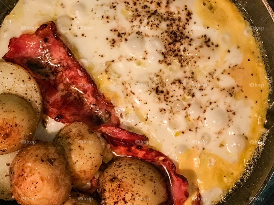 Fried eggs, shortcut bacon, baby potatoes halved closeup in fry pan