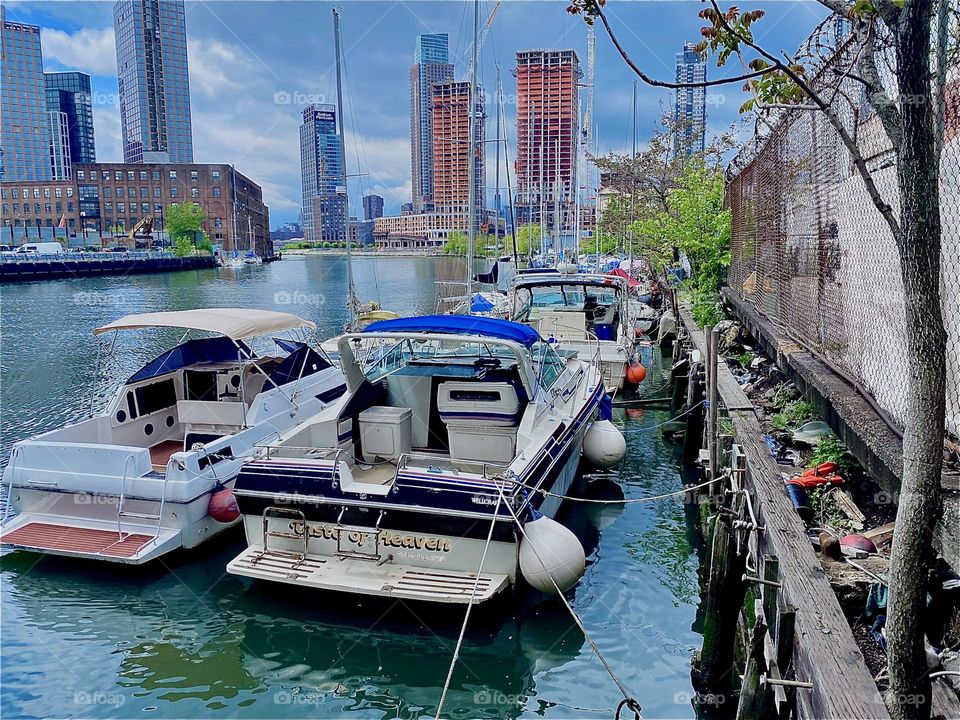 Various different kinds of boats are tied side by side to a wooden plank with boat hooks and ladders here at „Newtown Creek“ by the „Pulaski Bridge“. 2023. Hypnotic Productions