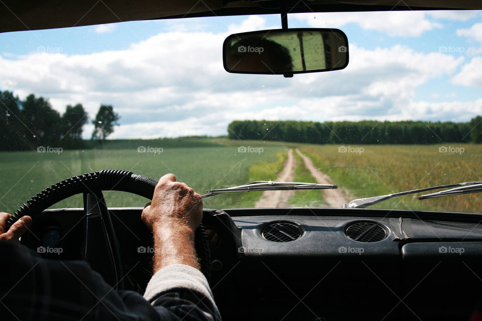 men's hands on the steering wheel of the car and ahead of the road in the field and forest