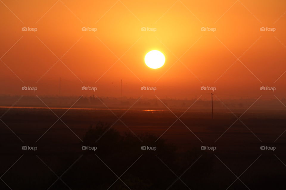 standing on a hilltop looking out over the valley as the sun rises in the sky painting it yellow, orange, and red. in the state's capital of Sacramento California.