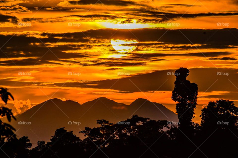 Beautiful sunset with trees and hills at foreground 