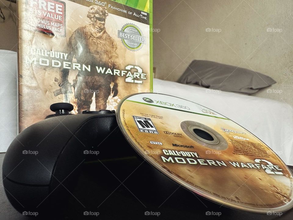 Video game disc modern warfare side by side with its box and Xbox controller closed up.